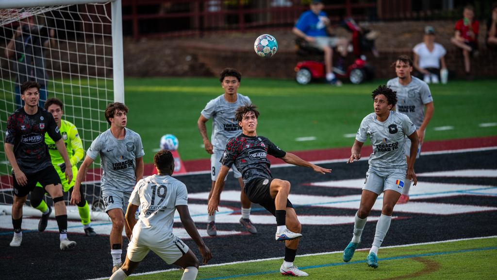 Hickory FC player, Ander Marticorena, stares at the ball above preparing to connect in front of Tobacco Road FC's goal.